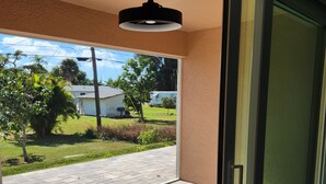 A room with a sliding glass door leading to a patio, a ceiling fan, and a view of a residential area with houses and trees. - 1 floor 3bedroom 2full bathroom  apartment in Bokeelia with AC 2vehicle garage (Bokeelia)