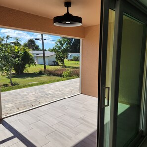 Ein Zimmer mit einer Schiebeglastür, die auf eine Terrasse führt, einem Deckenventilator und Blick auf eine Wohngegend mit Häusern und Bäumen.