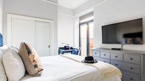 Ein Schlafzimmer mit Bett, Kissen, einem Schminktisch, einem Fernseher und einem Schreibtisch mit Stuhl.