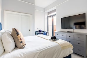 Ein Schlafzimmer mit Bett, Kissen, einem Schminktisch, einem Fernseher und einem Schreibtisch mit Stuhl.