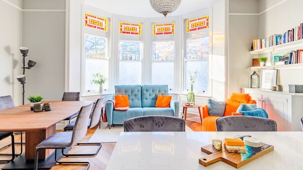Ein modernes Wohnzimmer mit Holzesstisch, blauem Sofa und orangen Kissen.