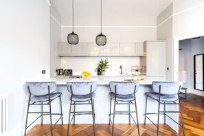 Eine moderne Küche mit einer zentralen Kochinsel, Barhocker, Pendelleuchten und einem Blumentopf.