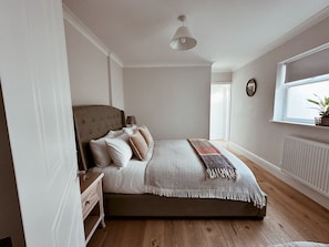 Ein Schlafzimmer mit Bett, Nachttisch, Lampe, Fenster und Blick ins Freie.