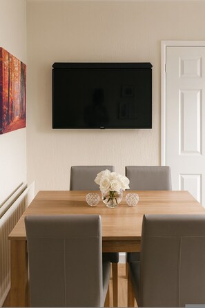 A dining table with chairs, a flat-screen TV mounted on the wall, and a painting on the wall. - Comfortable Two-bedroom Home in St Dials Cwmbran (Cwmbran)