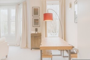 Ein Zimmer mit einem Holztisch, einer Bank, einem Schrank und einer Stehlampe.