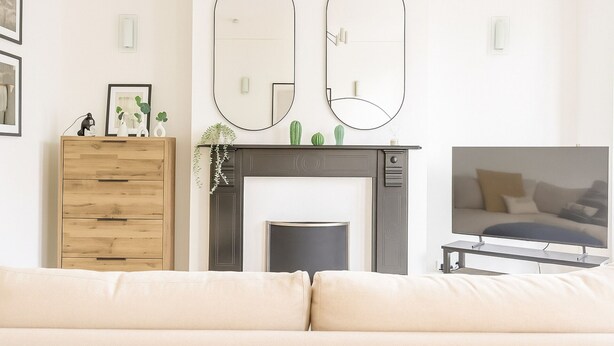 Een woonkamer met een bank, een open haard, twee spiegels, een televisie en een houten kast.