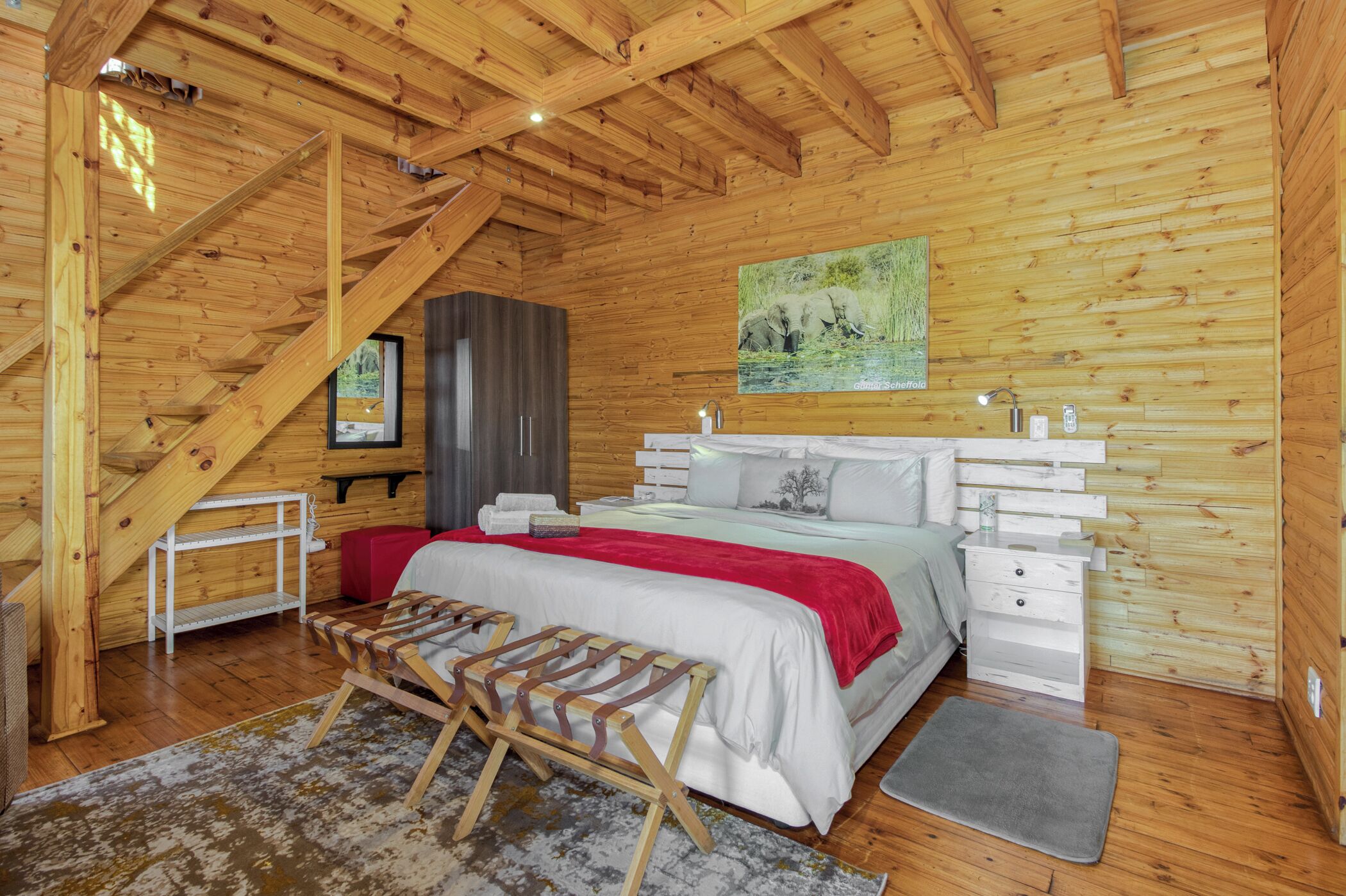 Camera da letto in una baita di legno, con un letto, comodini, una panca, una finestra e un quadro appeso al muro.