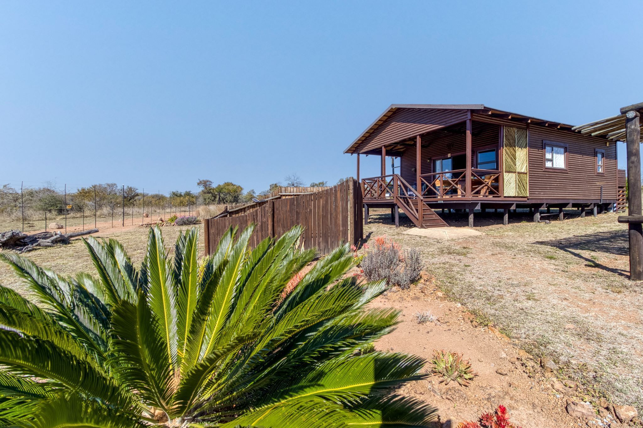 A wooden building with a porch, surrounded by dry vegetation and a clear sky.