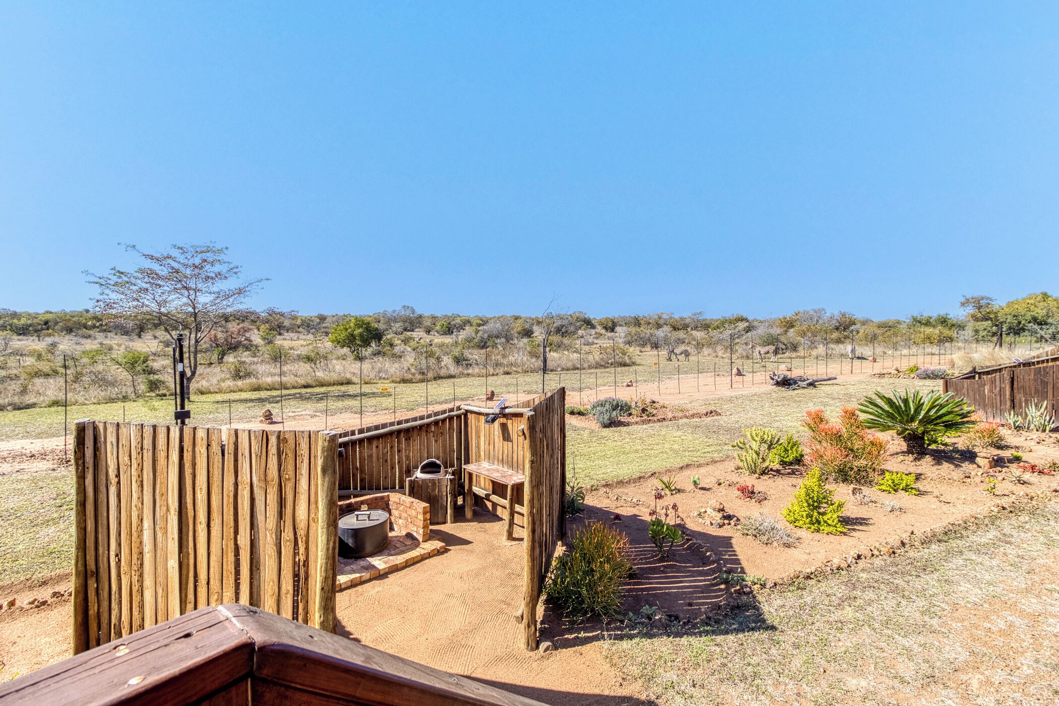 A fenced outdoor area with a wooden structure, a grill, and a garden with various plants.