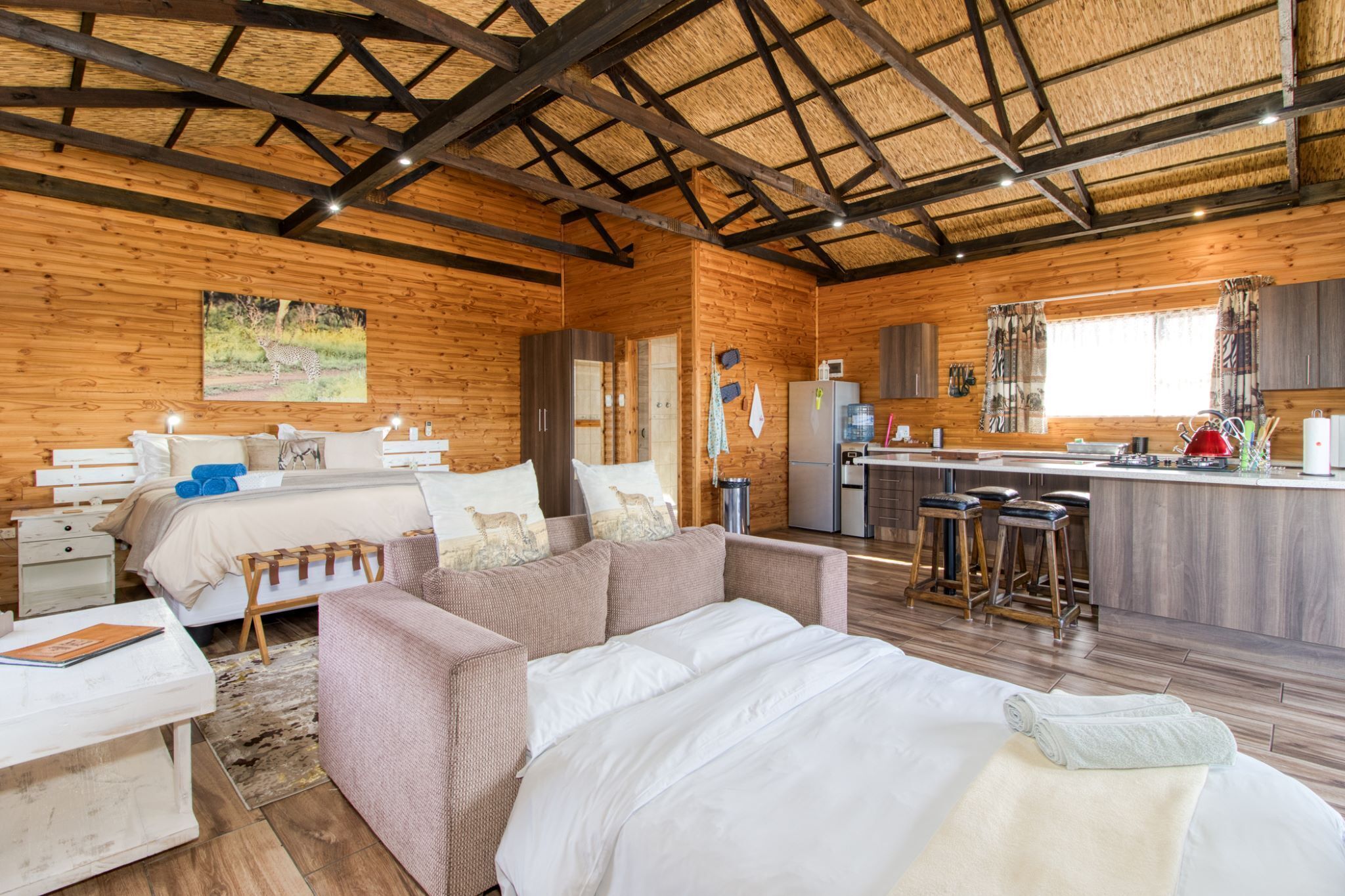 A log cabin interior with a bed, sofa, kitchen, and dining area.