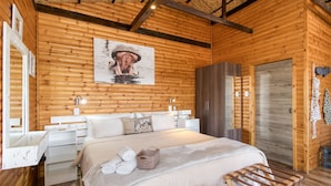 A wooden cabin-style bedroom with a bed, bedside tables, a wardrobe, and a painting on the wall.