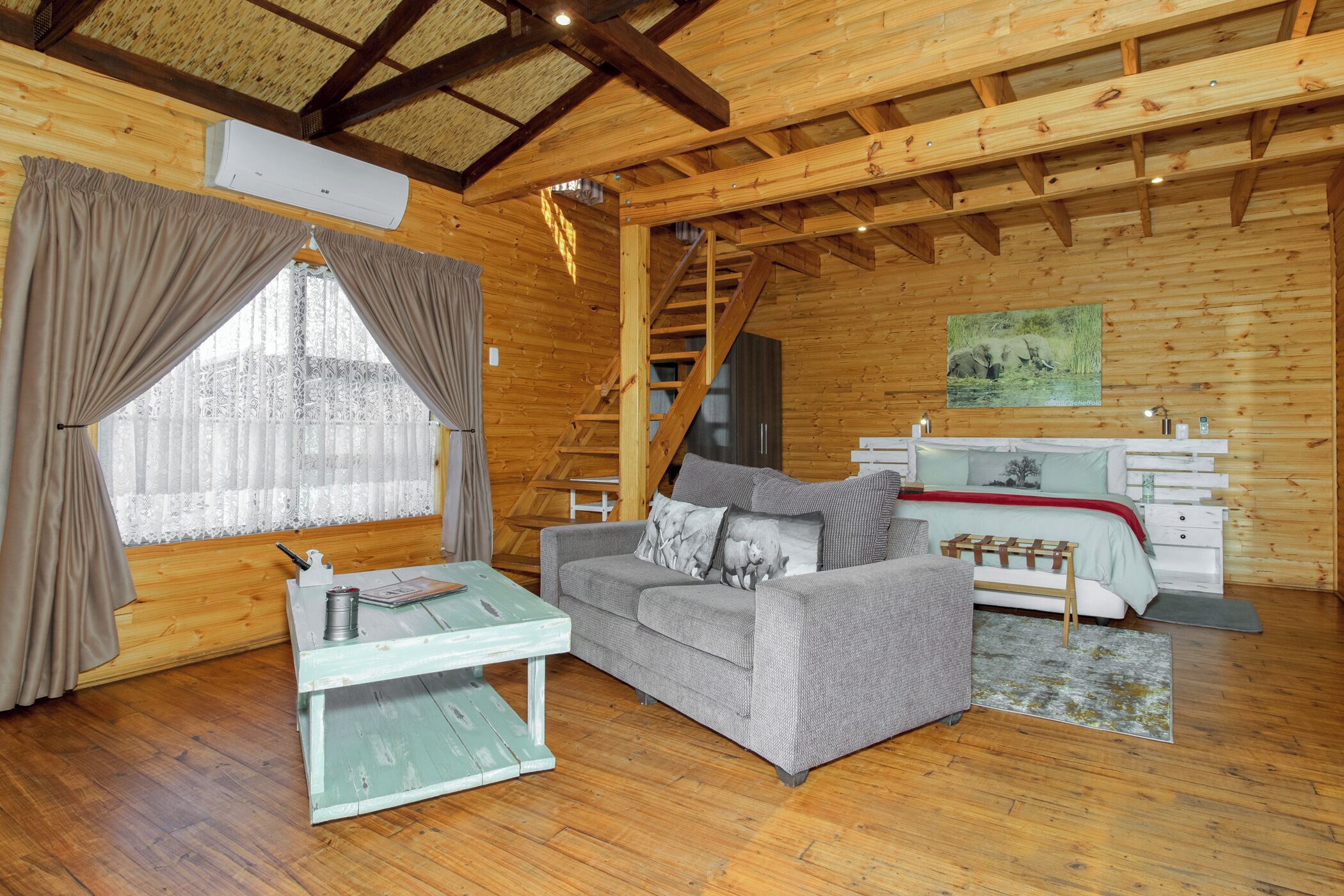 A wooden interior with a sofa, a small table, a staircase, and a bed with a headboard.