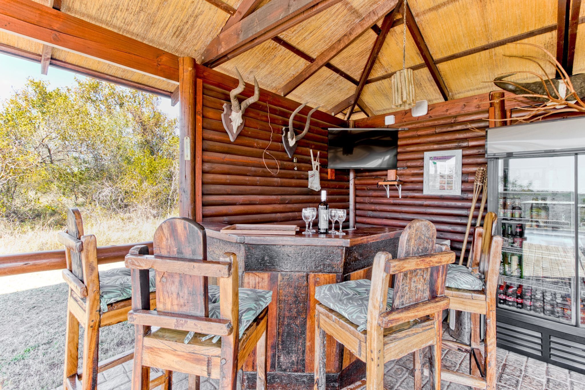 A rustic wooden cabin with a round table and chairs, a television, and a refrigerator stocked with beverages.