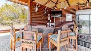 A rustic wooden cabin with a round table and chairs, a television, and a refrigerator stocked with beverages.