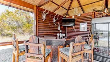 A rustic wooden cabin with a round table and chairs, a television, and a refrigerator stocked with beverages.