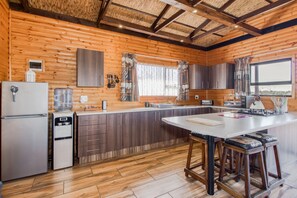 A modern kitchen with wooden walls, a large island, bar stools, and a water dispenser.