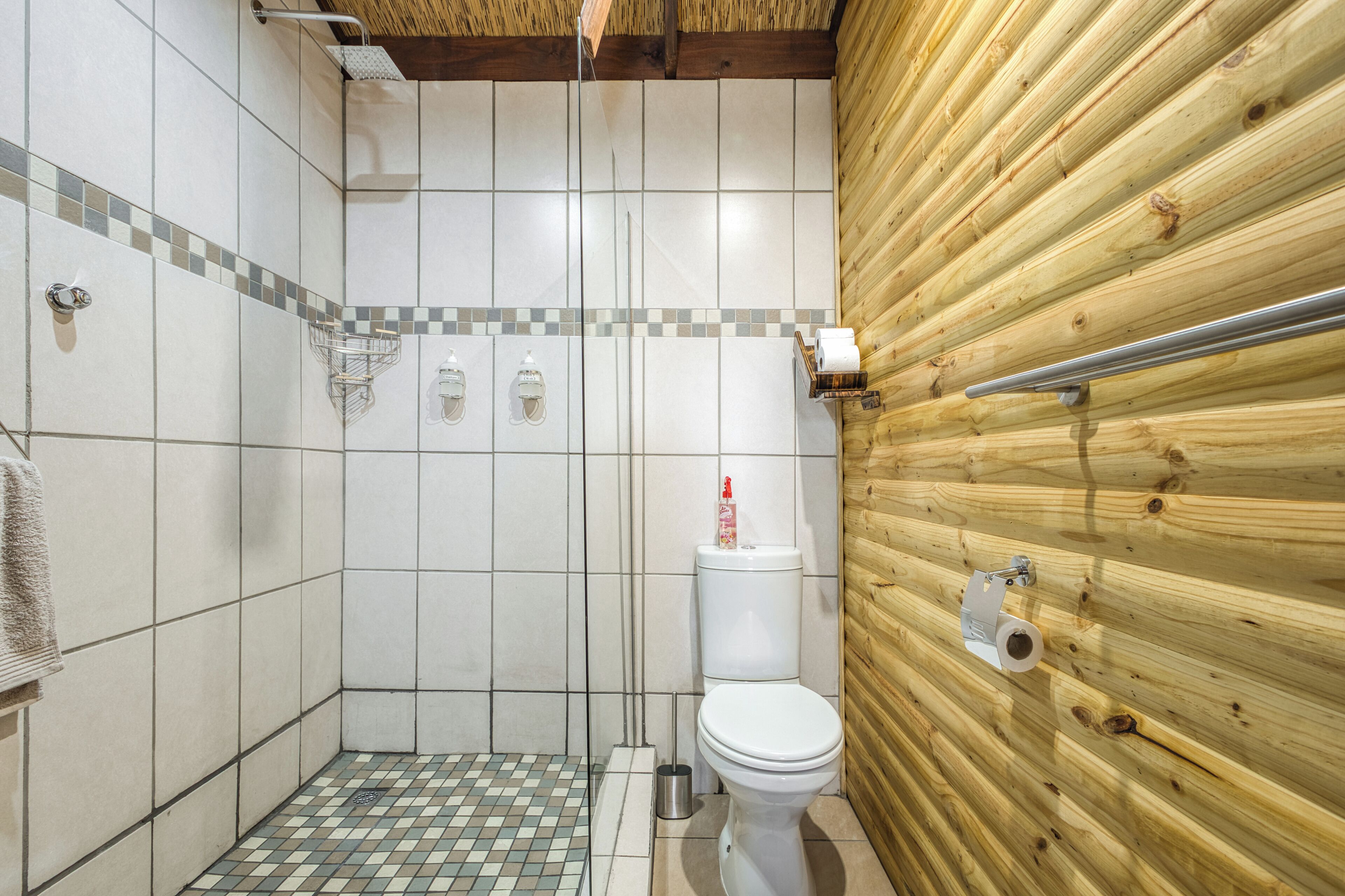 A small, tiled shower area with a wooden wall and a toilet.