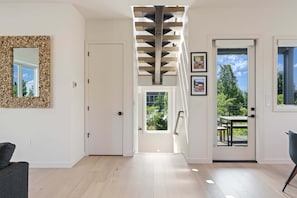 A modern interior with a staircase, a door leading to an outdoor area, and a framed mirror on the wall. - Peak and Pint - Perched Above Old Mill, Mountain Views, Walkable to Old Mill (Bend)