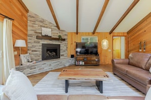 Un salón con chimenea de piedra, vigas de madera, televisor y sofá de cuero.