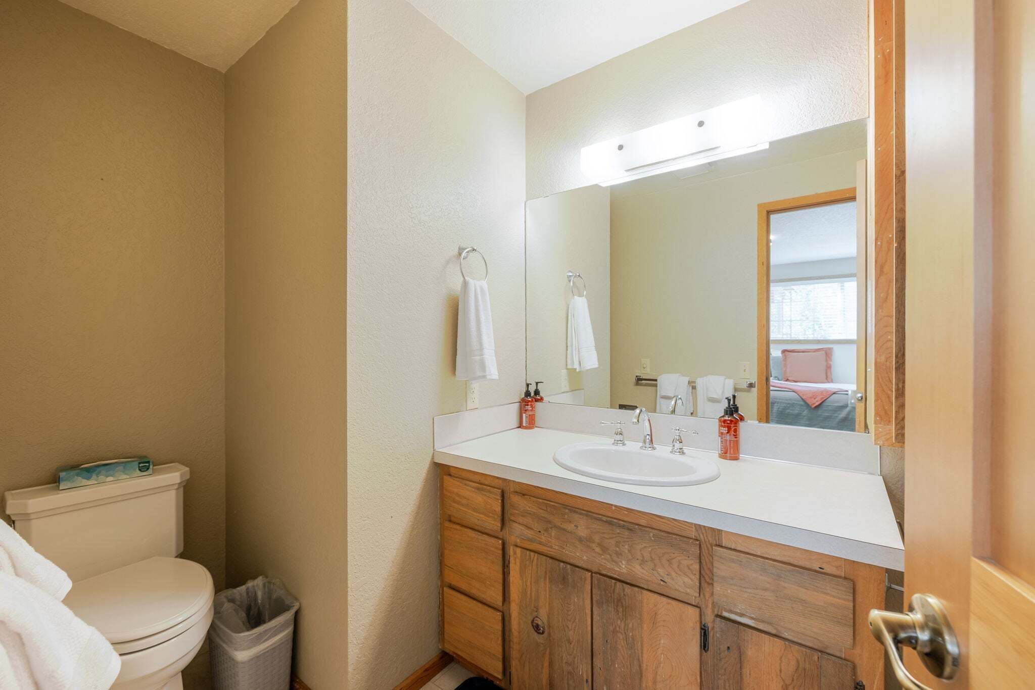 Een badkamer met toilet, wastafel, spiegel en houten kasten.