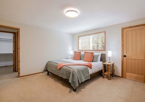 Un dormitorio con cama, mesita de noche, ventana con persianas, puerta y luz en el techo.