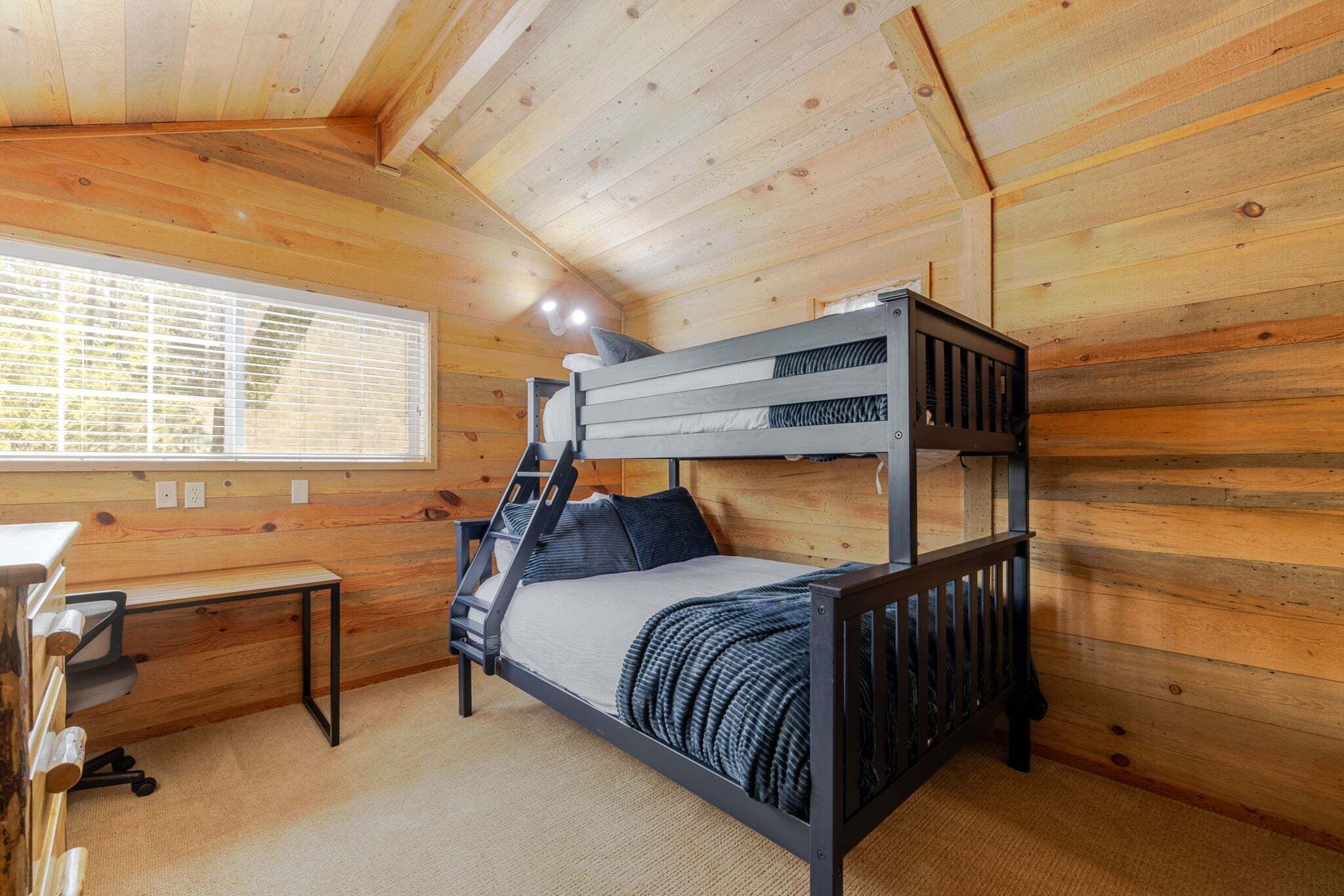 Un lit superposé dans une pièce en bois, avec un bureau et une fenêtre.