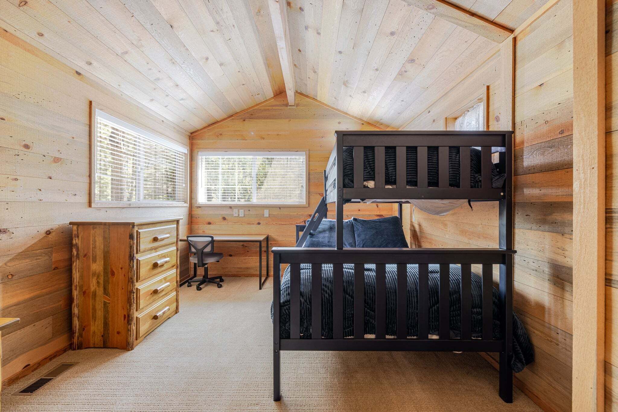 A cabin with a bunk bed, wooden walls, a desk, and a chair.