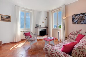 A living room with a sofa, a chair, a table, and a TV. - Cottage Antico Ulivo Lake Como View in Bellagio with Free Parking, AC & Patio (Bellagio)