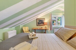 A bedroom with a bed, a chair, a table with a lamp, a radiator, and a window with curtains. - Cottage Antico Ulivo Lake Como View in Bellagio with Free Parking, AC & Patio (Bellagio)