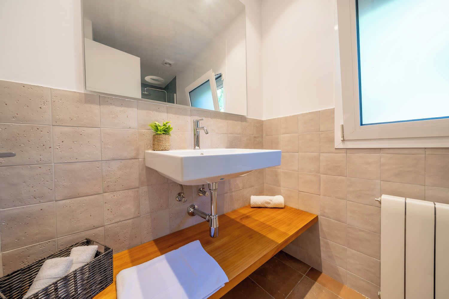 Ein Badezimmer mit einem weißen Waschbecken, einem Spiegel, einer kleinen Pflanze, einem Handtuch und einem Holzregal.