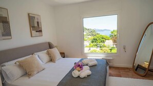 Um quarto com uma cama, uma janela com vista, um espelho e obras de arte na parede.