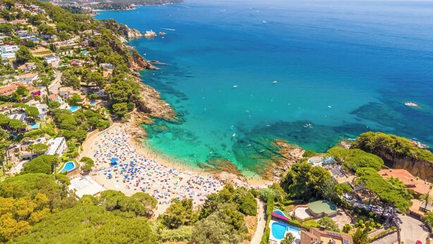Vista aérea de uma área costeira com praia, mar azul cristalino e vegetação ao redor.