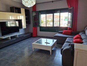 Ein Wohnzimmer mit Fernseher, Sofa, roten Kissen und einem Fenster mit Blick.