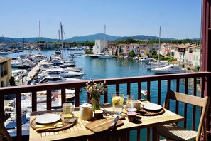 A balcony with a table set for dining, overlooking a marina with boats and colorful buildings. - Studio in the heart of Port Grimaud, 7 minutes from the beach + gorgeous view (Grimaud)