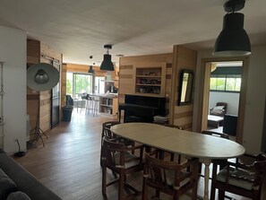 A spacious living area with a dining table, chairs, a sofa, a piano, and a kitchen in the background. - 4-Bedroom House—Pool—Private Parking, Air Conditioning, Historic City Center 10-Minute Walk Away (Bergerac)