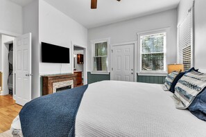 A bedroom with a bed, a television mounted on the wall, a fireplace, and a window with blinds.