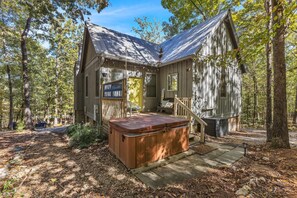 A rustic cabin with a hot tub, wooden deck, and a staircase leading to the entrance.
