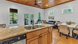 A kitchen with granite countertops, wooden cabinets, and a dishwasher. There is a dining area with a table and chairs, and a ceiling fan. - New! 2 bedroom/2 bath water access cabin at Lake Martin! Sleeps 8! (Dadeville)