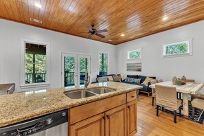 A kitchen with granite countertops, wooden cabinets, and a dishwasher. There is a dining area with a table and chairs, and a ceiling fan. - New! 2 bedroom/2 bath water access cabin at Lake Martin! Sleeps 8! (Dadeville)