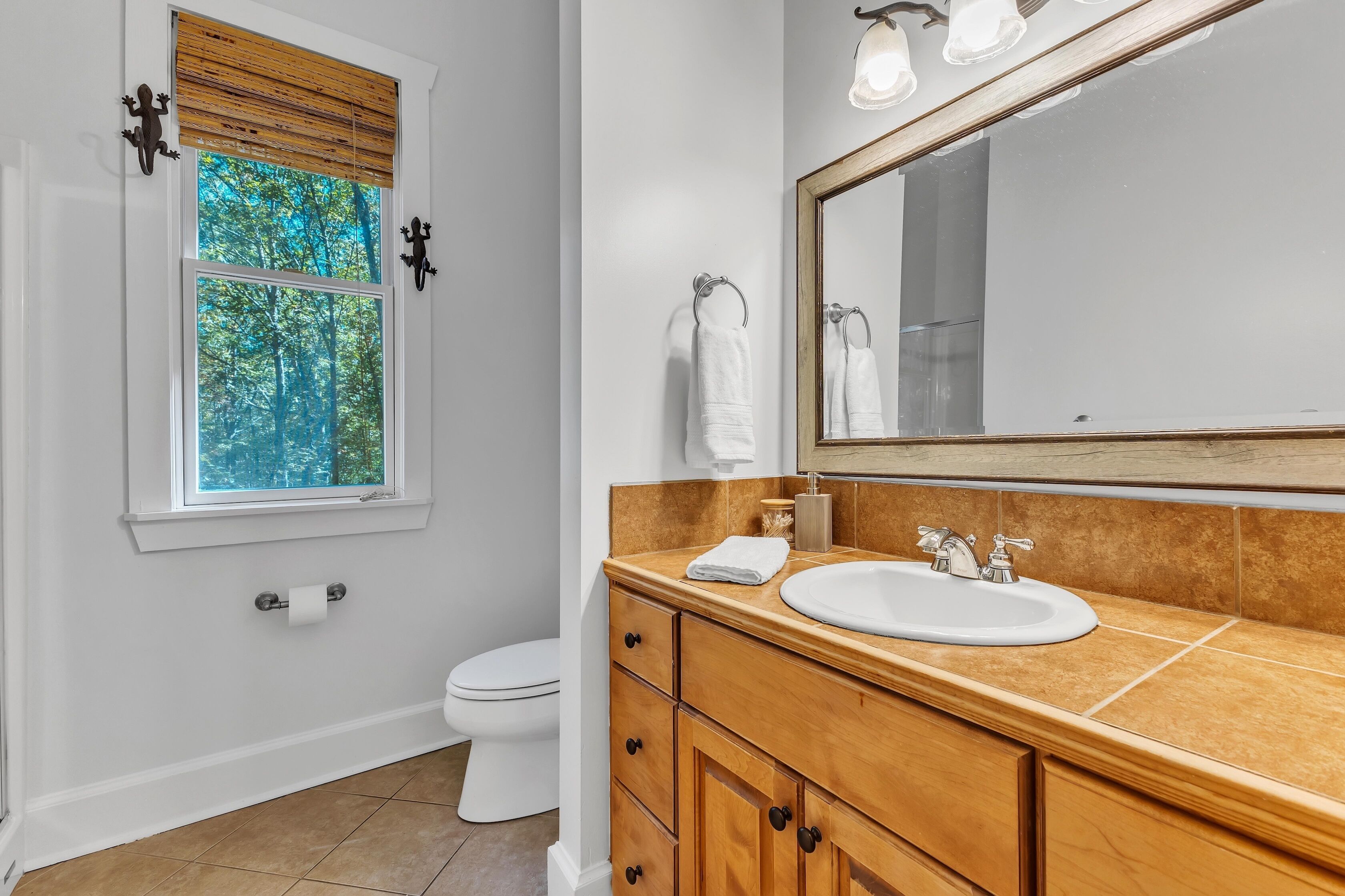 Un bagno con finestra, un water, un lavandino e mobili contenitori in legno.
