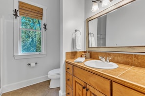 A bathroom with a window, a toilet, a sink, and wooden cabinets.