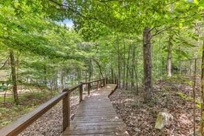 A wooden boardwalk through a forested area with trees and a fence on one side. - New! 2 bedroom/2 bath water access cabin at Lake Martin! Sleeps 8! (Dadeville)