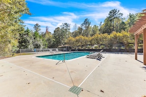 A swimming pool with a concrete deck, surrounded by trees and a pergola.