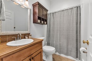 A bathroom with a white sink, wooden vanity, a mirror, a cabinet, a toilet, and a shower curtain.