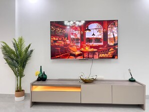 A modern living room with a large TV mounted on the wall, a wooden console table with decorative items, and a potted plant. - Shamms Goldpark homes (Nairobi)