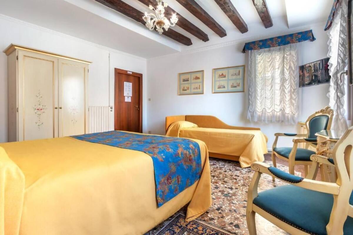 A room with two beds, a wooden chair, a wooden table, and a chandelier.