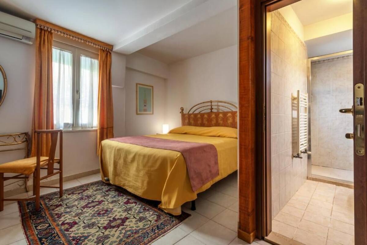 A bedroom with a bed, a chair, a window with curtains, a door leading to a bathroom, and a rug.