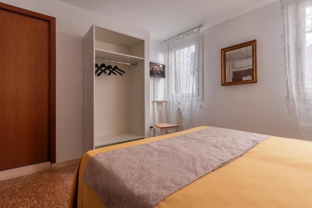 A bedroom with a bed, a wardrobe, a chair, and a window with curtains.