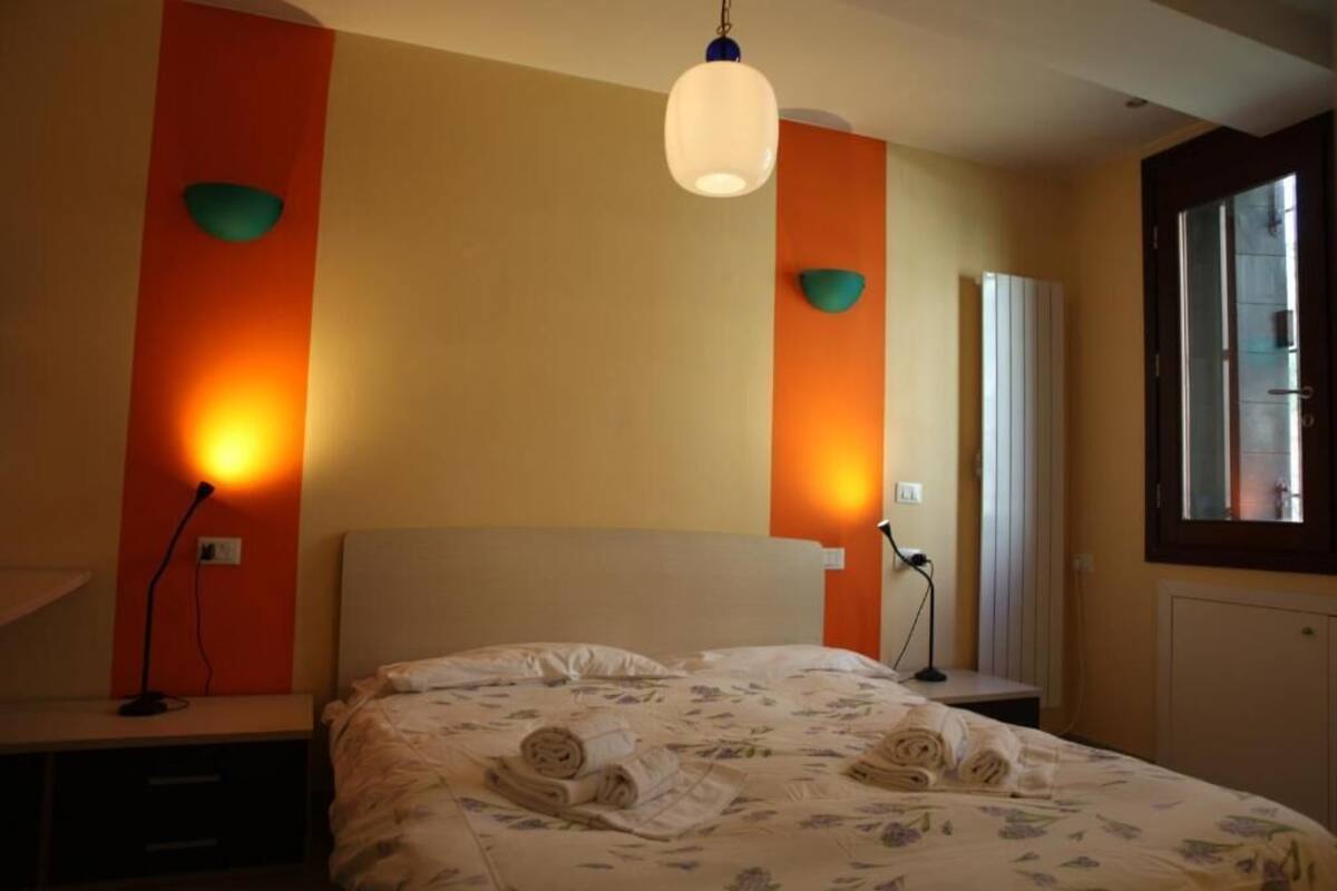 A hotel room with a bed, a desk, a lamp, and a window.