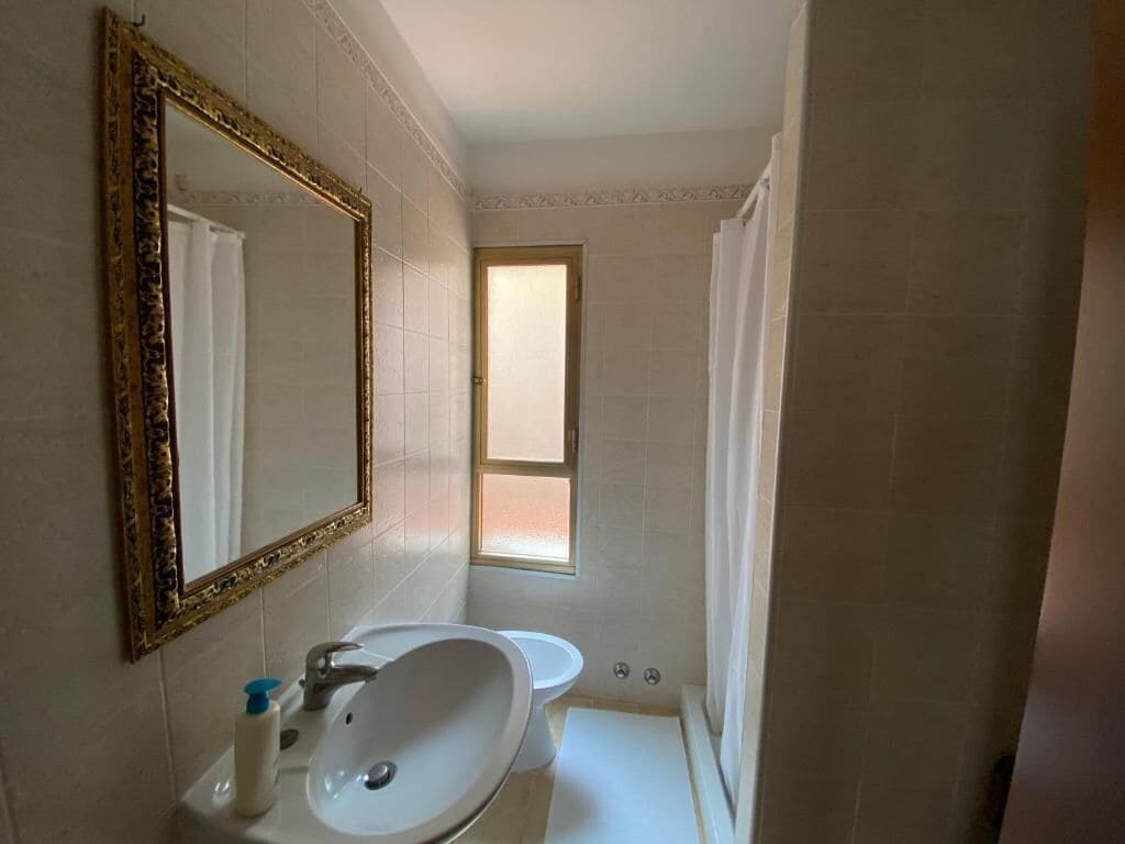 A bathroom with a large mirror, sink, toilet, and a window.